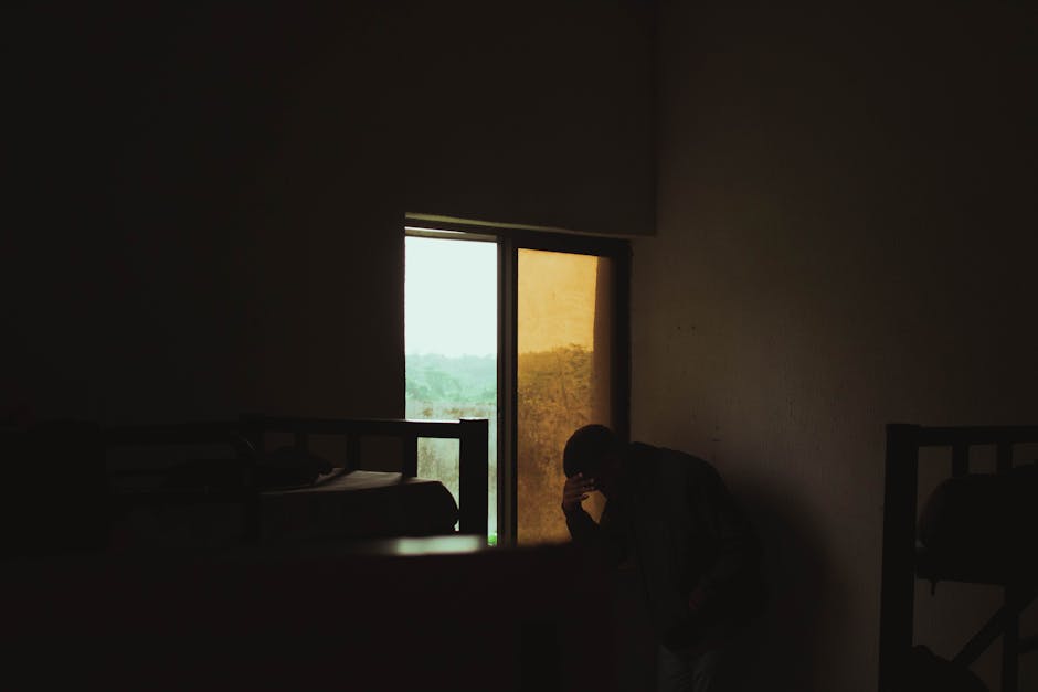 Depressed person sitting alone by a window in a dark room