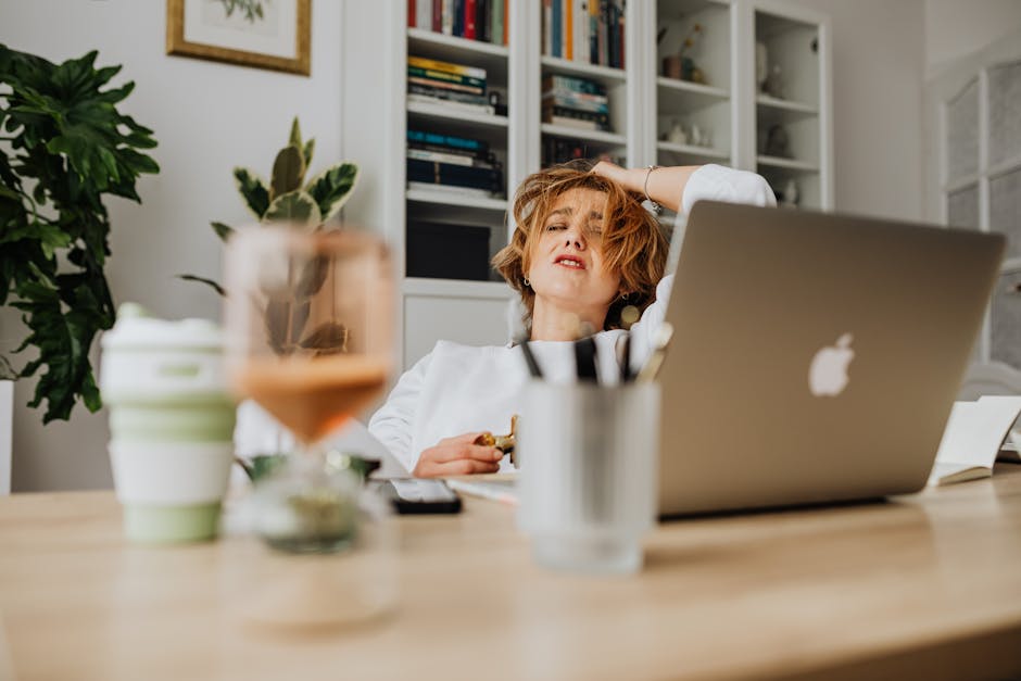 Person sitting at a desk looking overwhelmed by work and a laptop