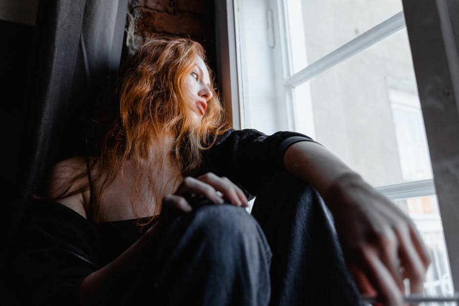 Person sitting alone by a window after a breakup