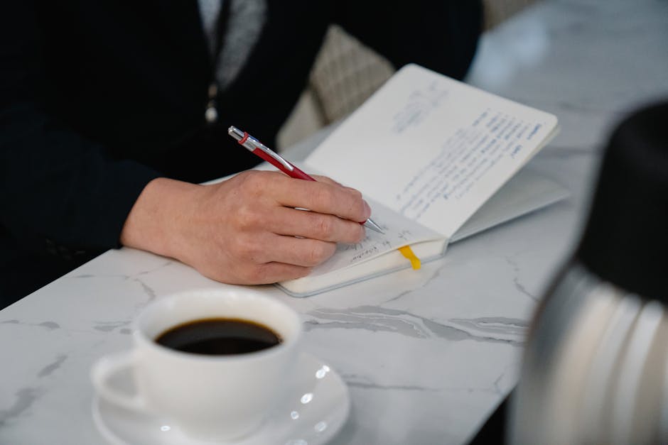 Person writing in a journal with a pen on a desk