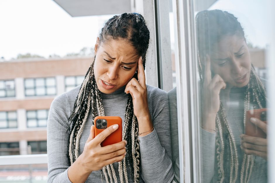 Woman looking at her phone with distress, representing digital monitoring and coercive control