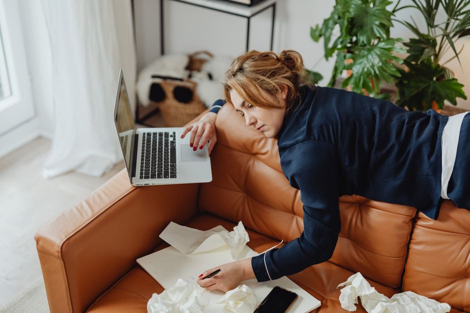 Person looking stressed and distracted at a desk with laptop and papers