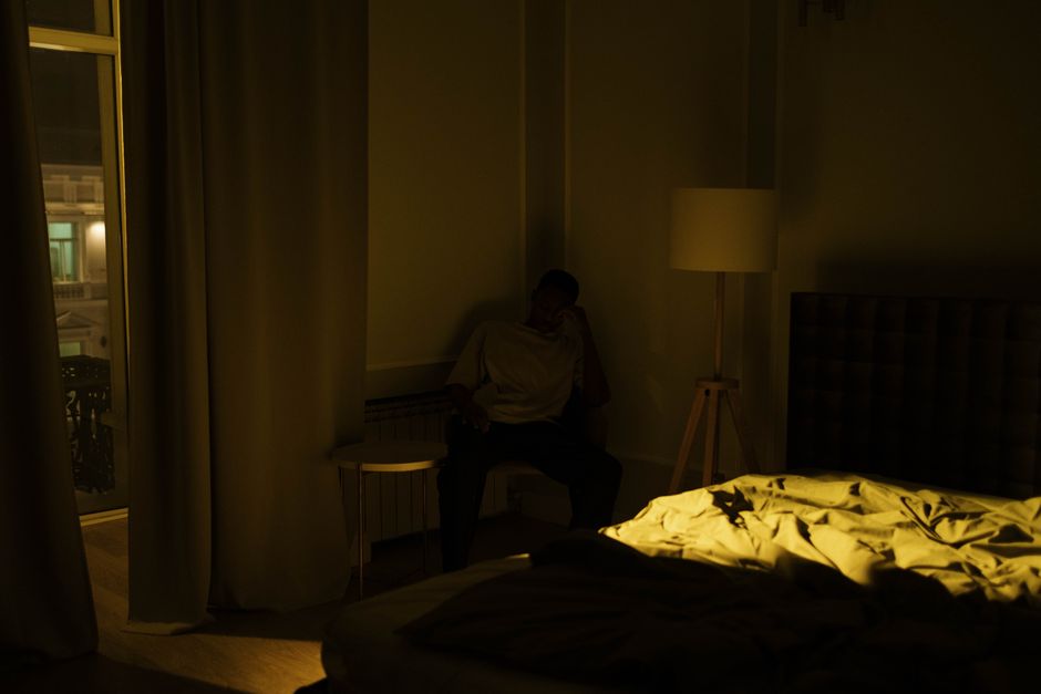 Tired person sitting on bed in a dark room looking exhausted