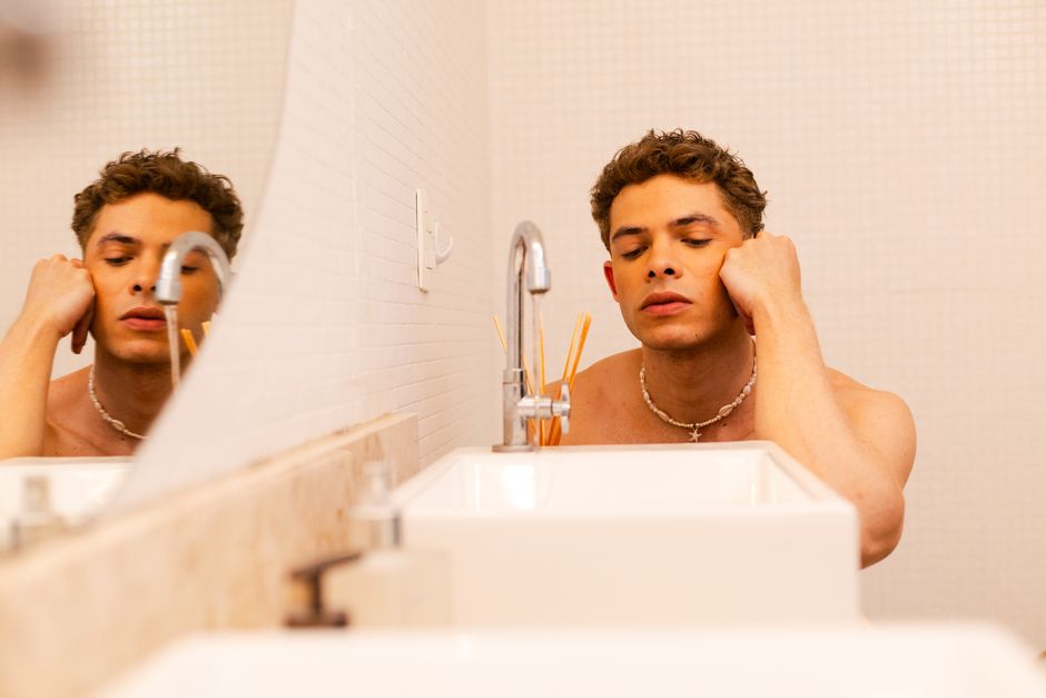 Personne se regardant dans un miroir avec une expression de doute, dans une salle de bain lumineuse