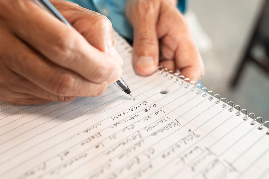 Person writing notes in a notebook to track repeated harmful behavior
