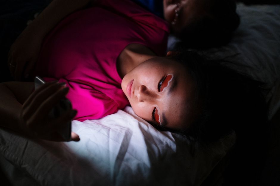 Person checking phone messages late at night in bed
