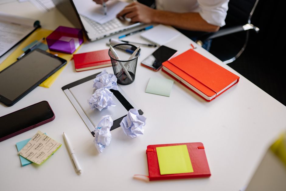 Overwhelmed person procrastinating with laptop and phone on a messy desk